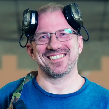 Ein lächelnder Mann mit Brille, Kopfhörern und Tarnkleidung hält ein Kontakt-Magazin in der Hand.